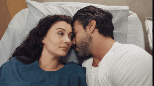 a man and a woman are laying in a hospital bed looking at each other