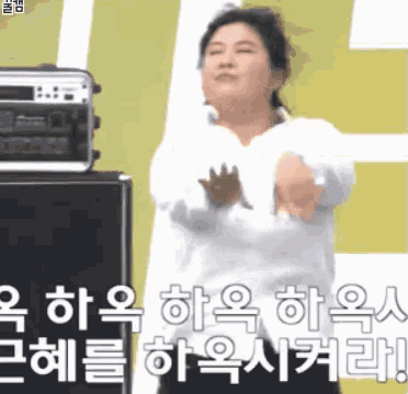 a woman in a white shirt is dancing in front of a microphone with korean writing on it .