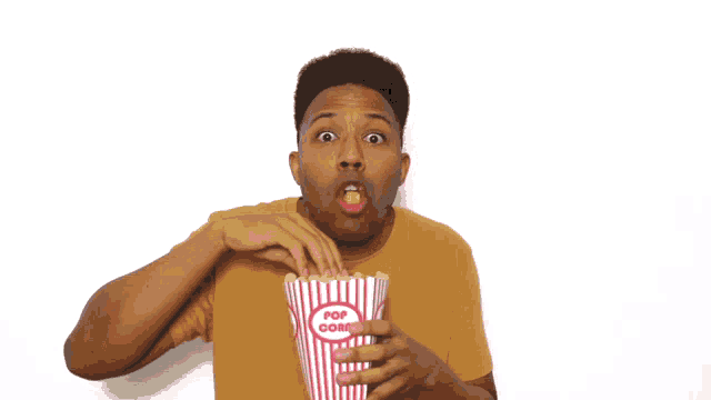 a man is eating popcorn from a red and white striped container