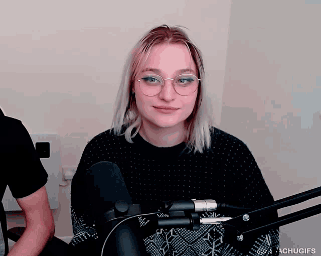a woman wearing glasses and a black sweater stands in front of a microphone with the hashtag chugifs
