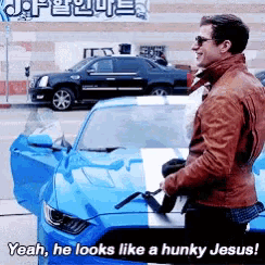 a man is standing next to a blue car with the words yeah he looks like a hunky jesus