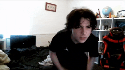 a young man in a black shirt is standing in front of a bed .