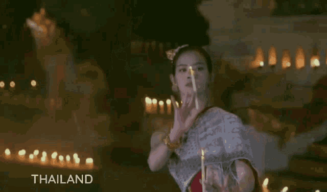 a woman is holding a lit candle in her hand and the word thailand is on the bottom