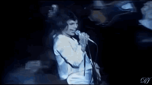 a man is singing into a microphone on a stage in front of a drum set .