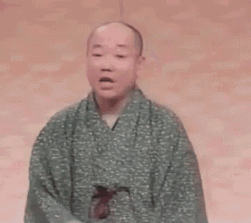 a bald man in a green robe is sitting on a stage and talking .