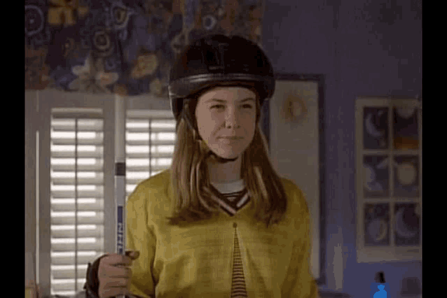 a girl wearing a helmet is holding a hockey stick .