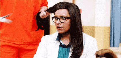 a woman wearing glasses and a lab coat is getting her hair done by a man in an orange uniform .