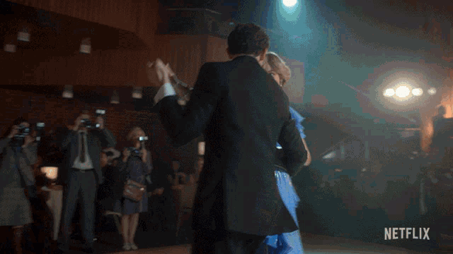 a woman in a blue dress is dancing with a man in a tuxedo in front of a netflix logo