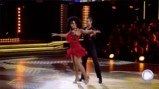 a woman in a red dress is dancing with a man in a black suit on a tv show