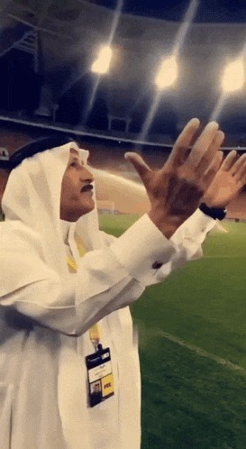 a man in a white robe holds his hands up in the air