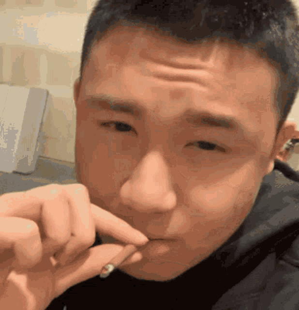 a close up of a man smoking a cigarette with his finger in his mouth