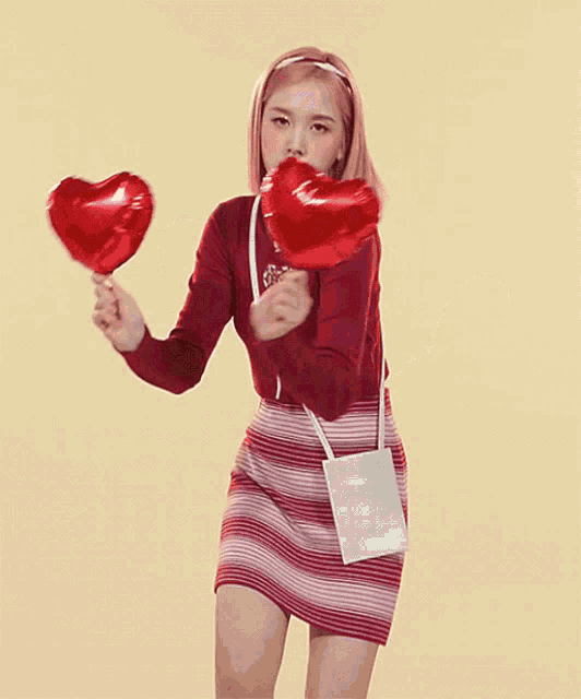 a woman in a red top and striped skirt holds two red heart shaped balloons