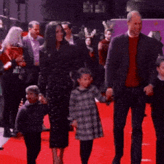 a group of people are walking on a red carpet holding hands