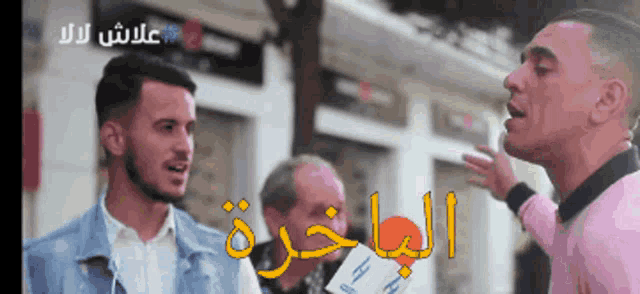a man in a pink shirt is talking to another man in front of a sign in arabic
