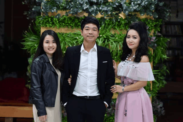 a man and two women pose for a picture in front of a wall of greenery