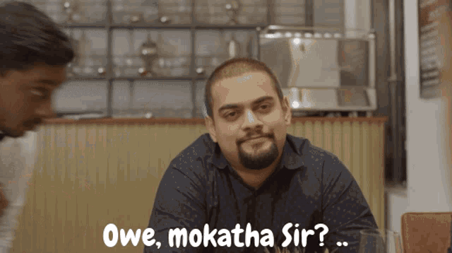 a man sitting at a table with the words owe mokatha sir