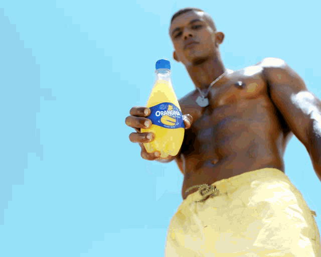 a shirtless man is holding a bottle of orange soda