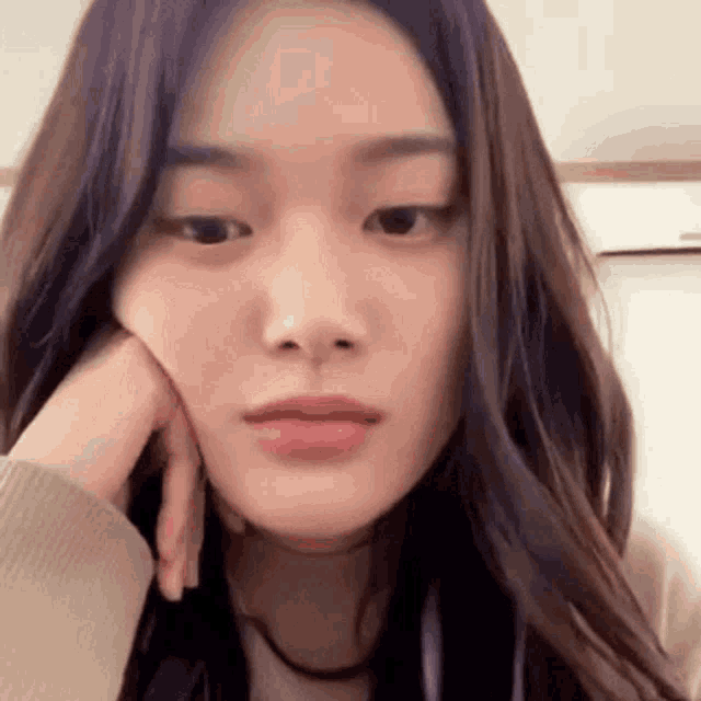 a close up of a woman 's face with her hand on her chin and looking at the camera .