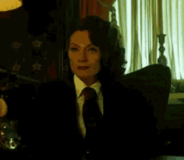 a woman in a suit and tie is sitting in a chair looking at a laptop .
