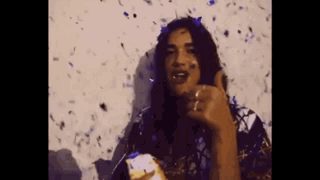 a woman is standing in front of a wall with confetti falling on her face .