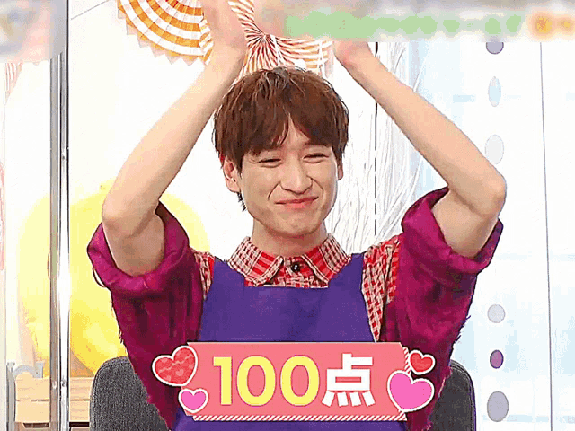 a man wearing a purple shirt and a blue apron holds up his hands and a sign that says 100 on it