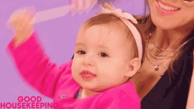 a woman is holding a baby girl in her arms and the baby is wearing a pink headband .