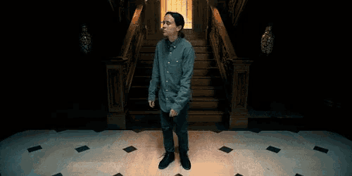 a man in a blue shirt and jeans is standing in front of a set of stairs