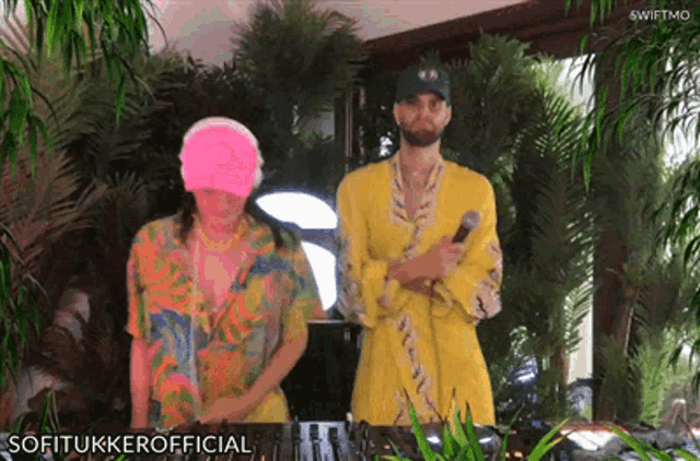 a man in a yellow robe is holding a microphone while a woman in a pink hat stands behind him
