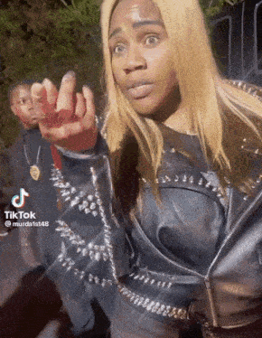 a woman in a black leather jacket with spikes on the sleeves is giving the middle finger