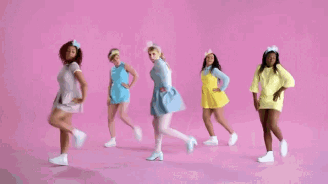 a group of women are dancing in front of a pink wall .