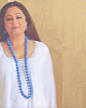 a woman wearing a white shirt and a blue necklace is smiling
