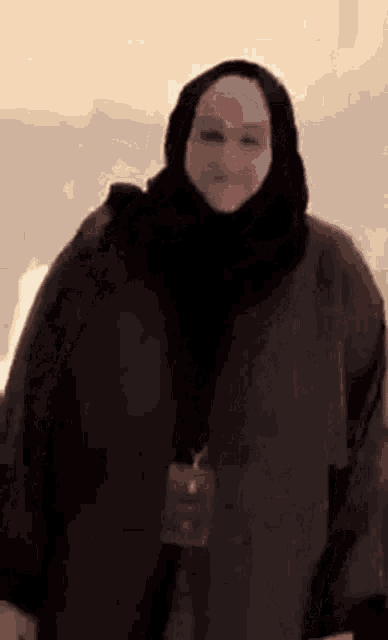 a woman wearing a black hijab and a black coat is standing in front of a wall .