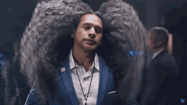 a man with very long hair is wearing a blue suit and a lanyard around his neck