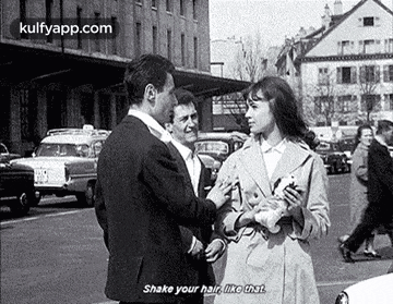 a black and white photo of a man shaking a woman 's hair in a street .