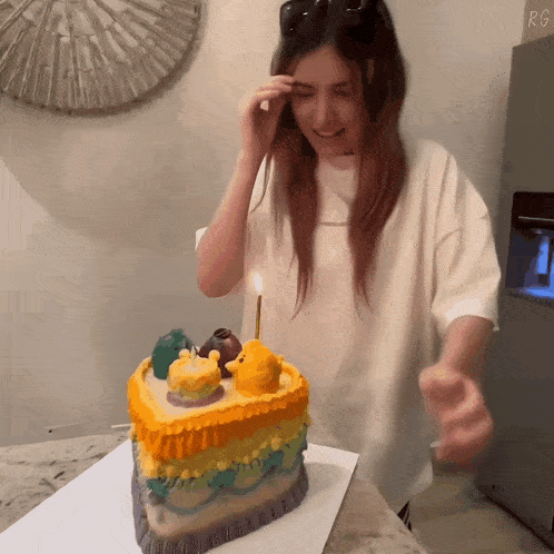 a woman stands in front of a birthday cake with a candle lit up