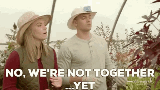 a man and a woman are standing next to each other in a greenhouse and talking .