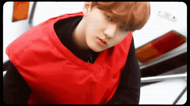 a young man wearing a red vest and black shirt looks at the camera