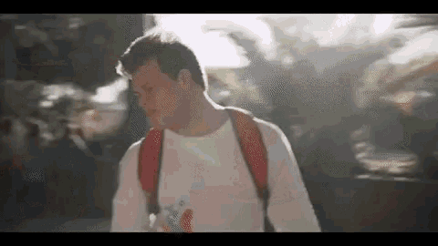 a man wearing a white shirt and a red backpack is walking down a street .