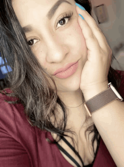 a woman wearing a maroon shirt and a brown watch holds her hand to her face