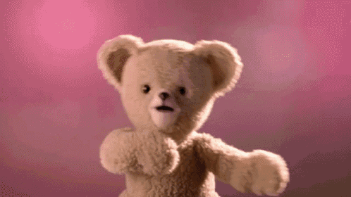 a teddy bear is standing in front of a pink background and looking at the camera .