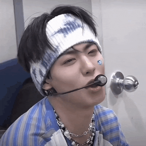 a man wearing a tie dye headband and a necklace with a microphone in his mouth