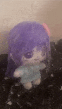 a stuffed doll with purple hair and a blue shirt is sitting on a black surface .