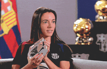 a woman wearing a black shirt with a fcb logo on it holds a trophy