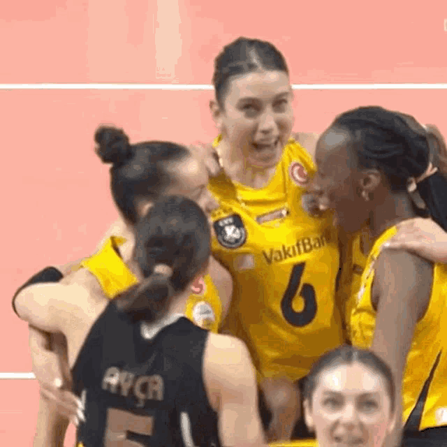 a group of volleyball players are hugging each other on a court .