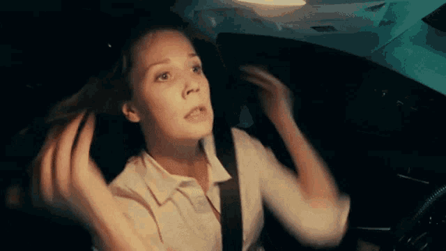 a woman is sitting in the driver 's seat of a car holding her hair .