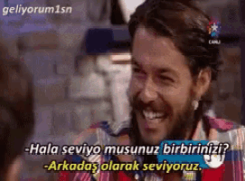 a man with a beard is smiling and says " hala seviyo musunuz birbiriniz ? "
