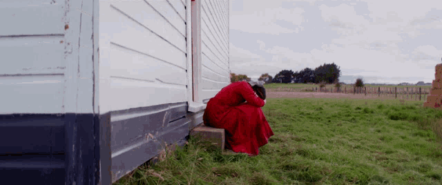 a woman in a red dress sits on the side of a white building