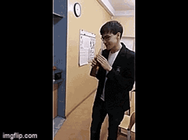 a man in a suit is standing in a hallway holding a book and drinking from it .
