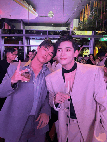 two men standing next to each other with one holding a glass of beer and the other holding a glass of champagne