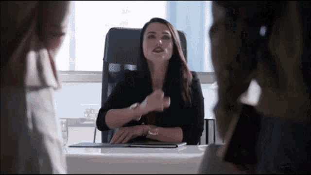 a woman is sitting at a desk in an office and talking to a man .